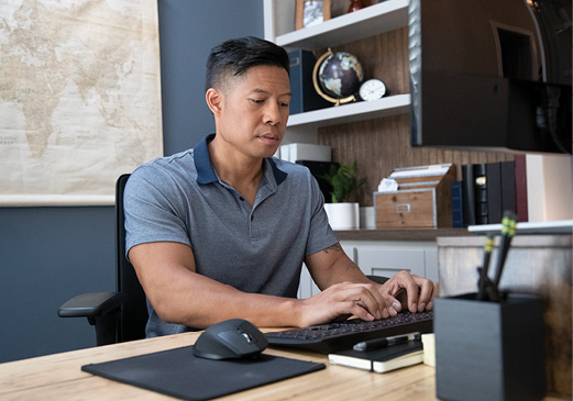 man sitting at a desk while typing on a keyboard